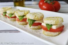 small sandwiches with tomatoes and mozzarella on a white platter next to some olives