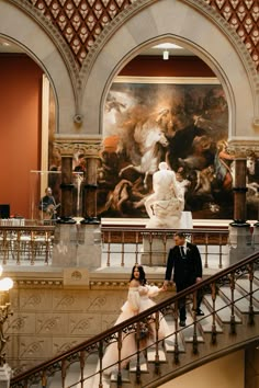 a man and woman standing on top of a staircase in front of a large painting