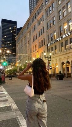 a woman standing on the side of a street next to tall buildings and traffic lights