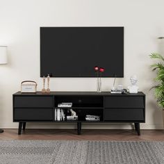 a living room with a black entertainment center and potted plants on the sideboard