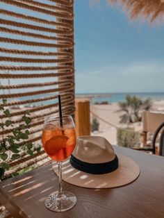 a hat sitting on top of a wooden table next to a glass filled with liquid