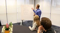 a man standing in front of a whiteboard giving a presentation to people sitting at a table