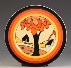 an orange and black plate with a tree painted on the side, in front of a gray background