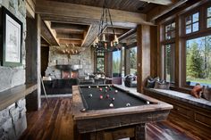 a pool table in the middle of a living room with wood flooring and large windows