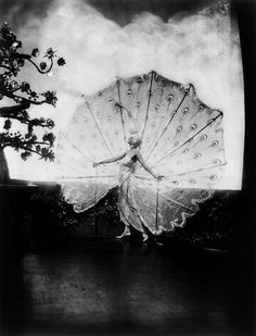 a black and white photo of a woman holding a large umbrella in front of a tree