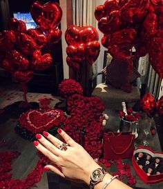 a woman's hand with red manicures on her nails next to heart shaped balloons