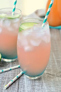 two glasses filled with pink lemonade, lime and ice next to some straws