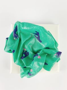 a square white plate topped with a green and purple scarf on top of it's side