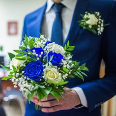 a man in a blue suit holding a bouquet of white and blue flowers on his lapel