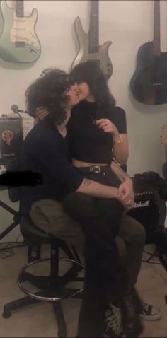 two women sitting on a chair in front of guitars, one is kissing the other's cheek