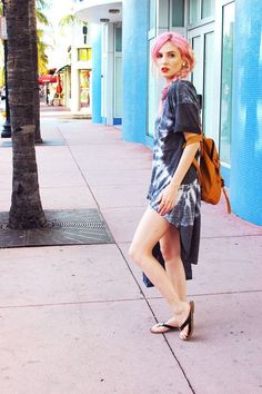 a woman with pink hair is standing on the sidewalk in front of a blue building