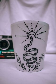 a cup with a snake on it sitting next to some books and a digital camera