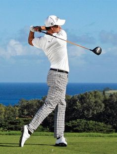 a man swinging a golf club on top of a lush green field next to the ocean