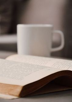 an open book sitting on top of a table next to a cup