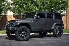 a black jeep parked in front of a tree on the side of a road next to a brick building