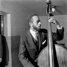 a black and white photo of a man in a suit playing the bassoon while another man looks on