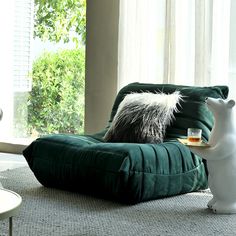 a white bear sitting on top of a green chair in front of a window next to a cup