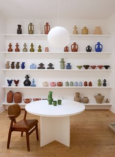 a white table and chairs in a room with shelves filled with vases on the wall