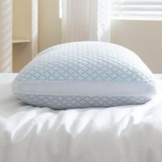 a close up of a pillow on a bed with white sheets and curtains in the background