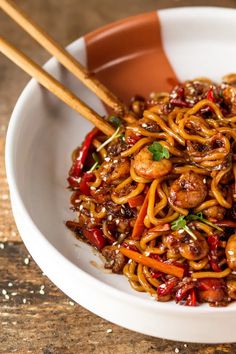 a white bowl filled with noodles and meat on top of a wooden table next to chopsticks