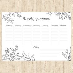 the weekly planner is shown on a wooden surface with flowers and leaves in black ink