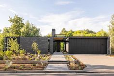 a modern house in the woods surrounded by trees and shrubs, with an entry way leading to it