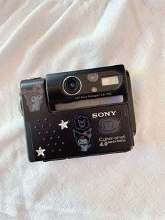 a camera is laying on top of a white sheet and has stickers on it