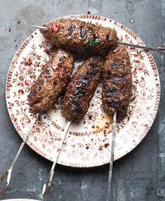 two steaks on skewers sitting on a white and brown plate with utensils