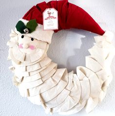 a white wreath with a red santa hat on it and a tag hanging from the front