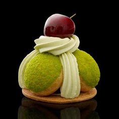 a green cupcake with white icing and a cherry on top, sitting on a wooden plate