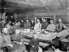 a group of people sitting around a table with food and drinks on it in an old log cabin