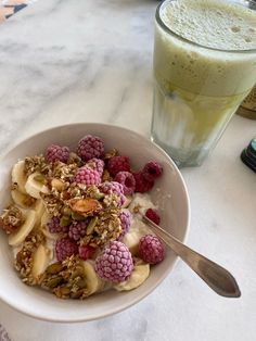 a bowl filled with granola and raspberries next to a drink