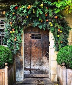 an old wooden door decorated with greenery and fruit hanging from it's sides