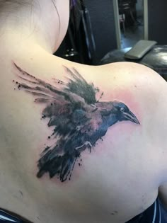 the back of a woman's shoulder with a black and grey bird on it