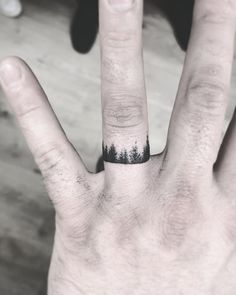 a person's hand with a ring on it and trees in the middle of their fingers