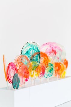 colorful lollipops sitting on top of a white box in front of a white wall