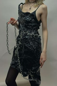 a woman in a black dress with chains around her neck and hands behind her back