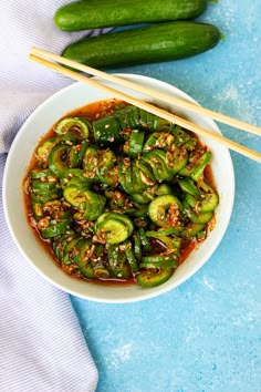 a white bowl filled with green vegetables and chopsticks on top of a blue surface