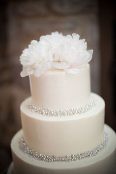 a wedding cake with white flowers on top and silver beaded trim around the edges