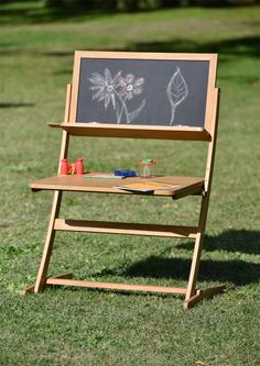 a wooden easel sitting on top of a grass covered field next to a chalkboard