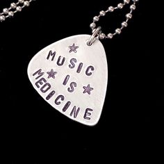 a guitar pick with the words music is medicine on it hanging from a ball chain