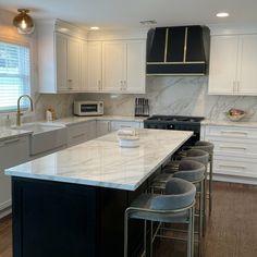 a kitchen with white cabinets and marble counter tops, an island in the middle is surrounded by bar stools