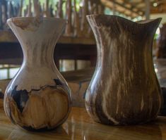 two vases sitting on top of a wooden table next to each other, one is brown and the other is white