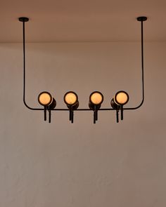 four lights are hanging from the ceiling in front of a white wall and below them is a light fixture