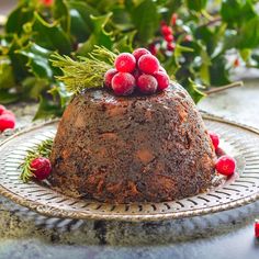 a chocolate cake with cranberries and greenery on top sits on a plate