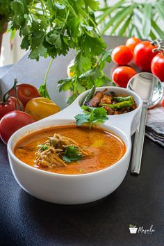 a bowl of soup on a table with tomatoes and other food items in the background