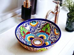 a colorful bowl sink sitting on top of a white counter next to a green plant