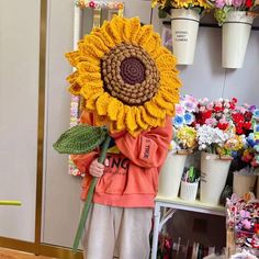 a person holding a giant sunflower in front of a flower shop