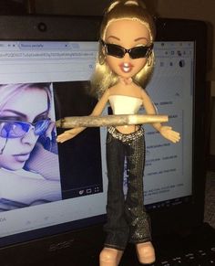 a barbie doll holding a stick in front of a computer screen with an image of a woman on it