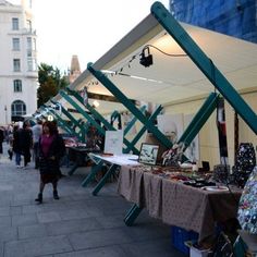 an outdoor market with people walking around and tables covered in cloths on the sidewalk